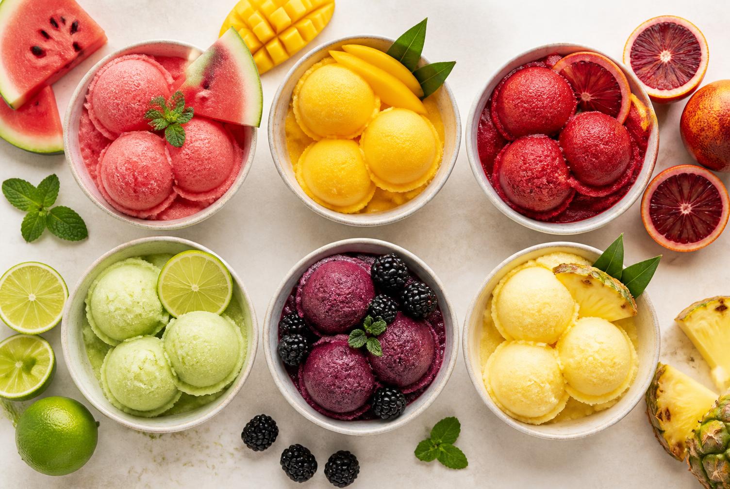 Six bowls of colorful fruit sorbet arranged with fresh fruit